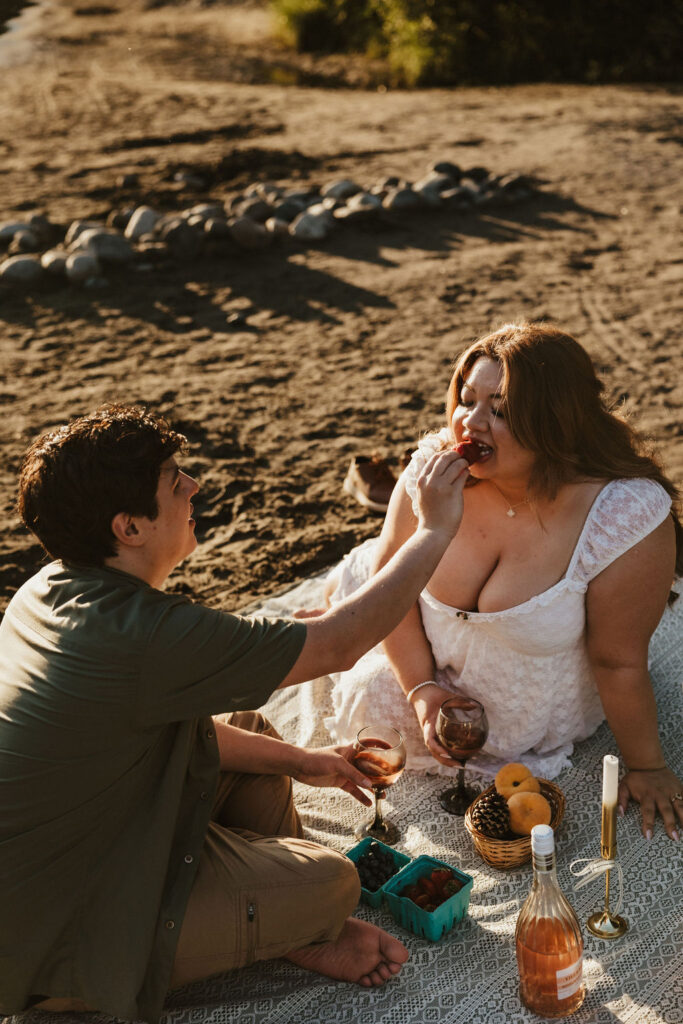 A romantic engagement session picnic on a sandy beach during golden hour photographed by Wilder Photography